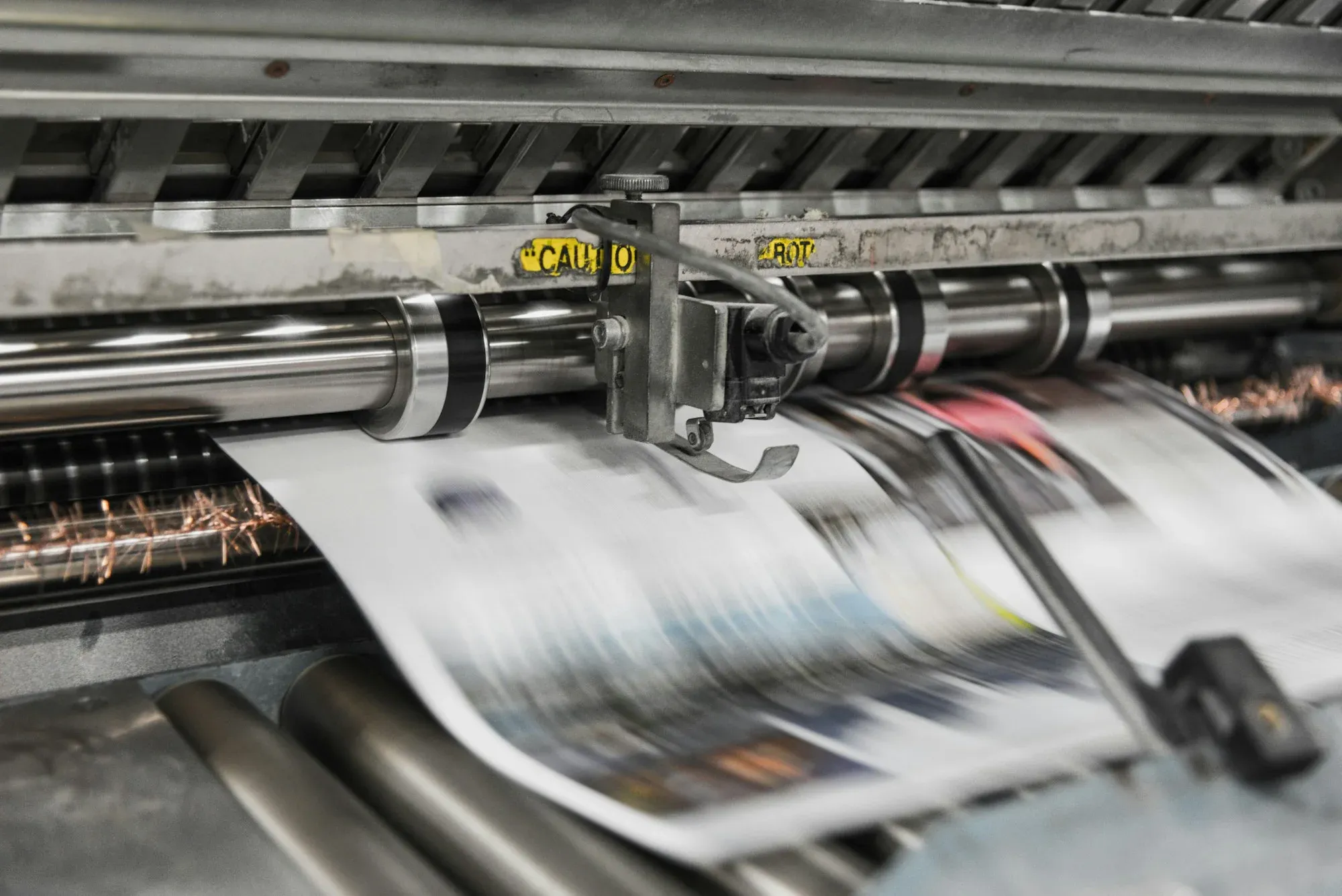 Paper moving through the rollers of a printing press.