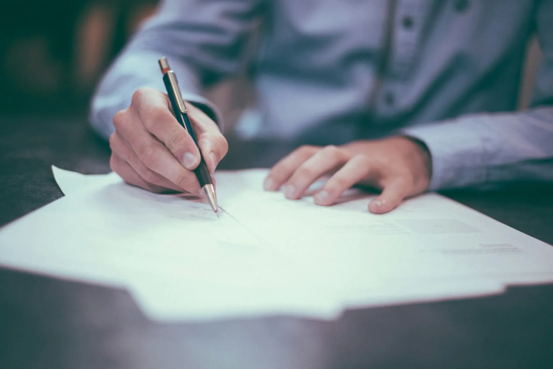 A person signing a paper document with a pen.