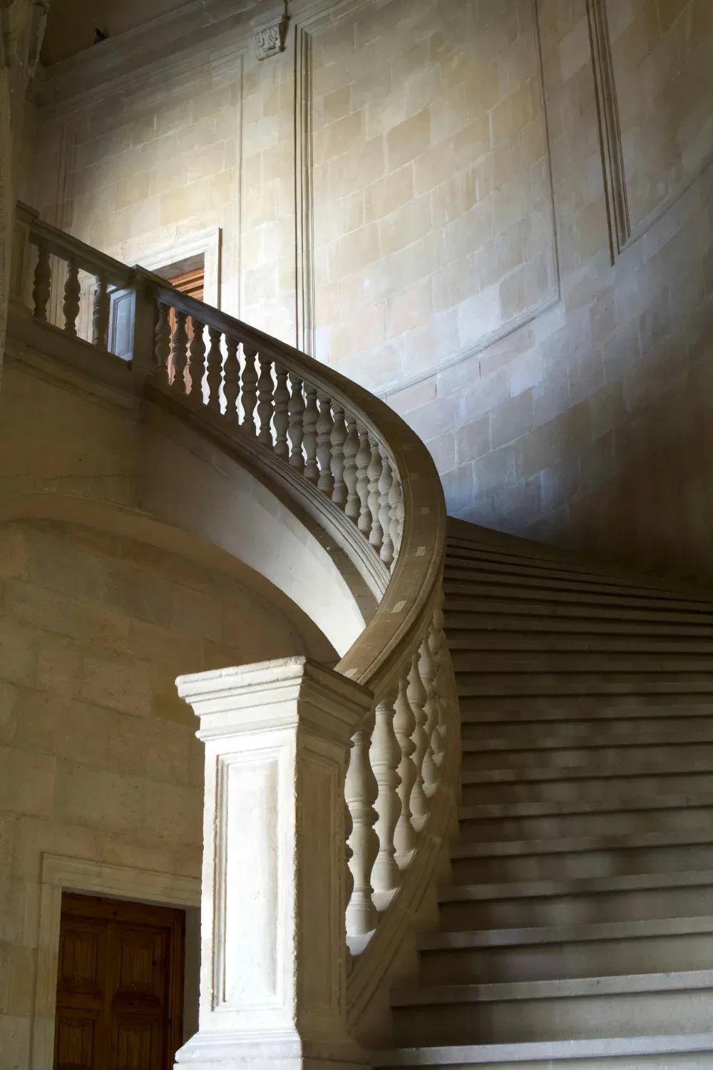 A curved limestone staircase and balustrade in soft side light.